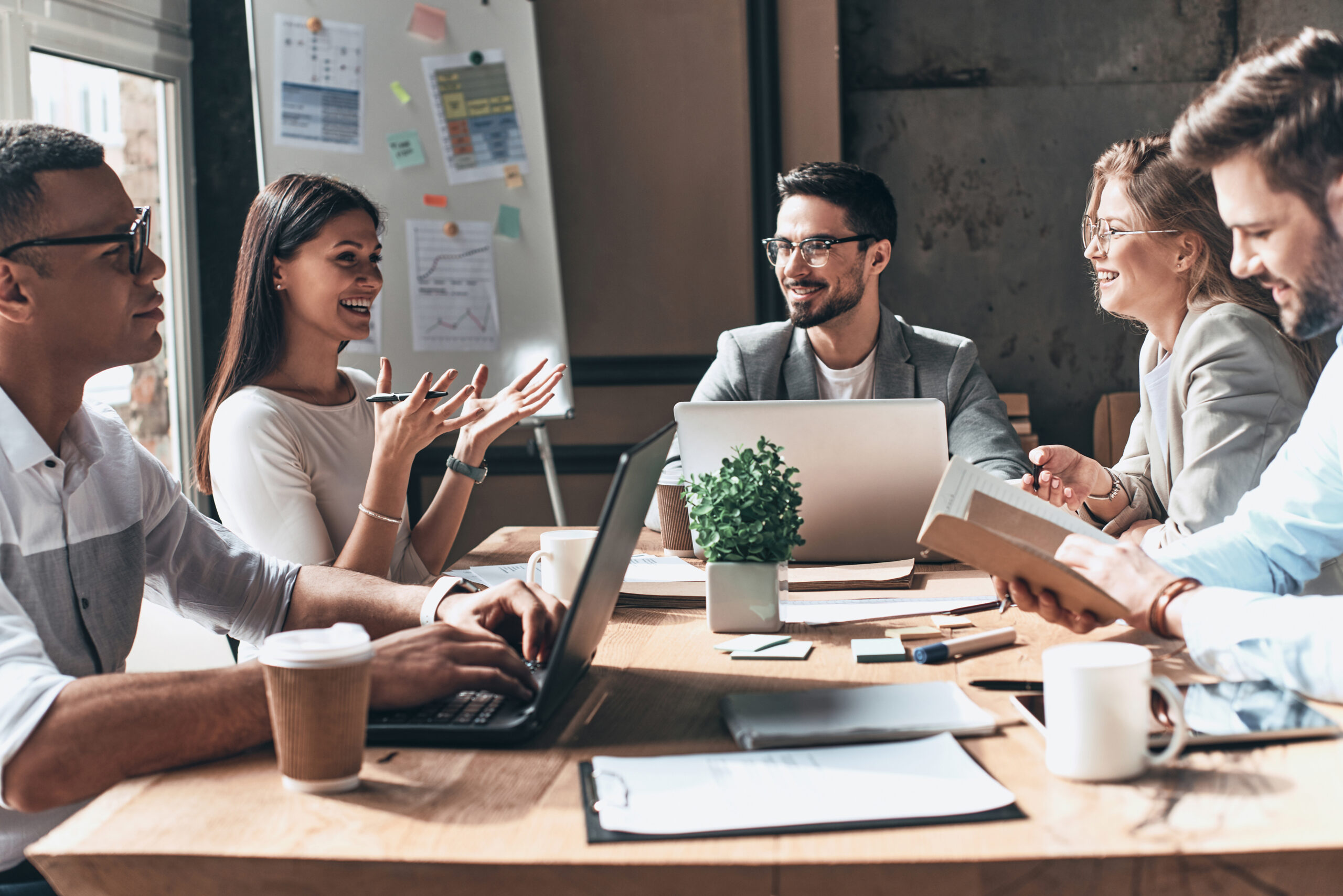 Group of young modern people in smart casual wear discussing business and smiling while sitting in the creative office